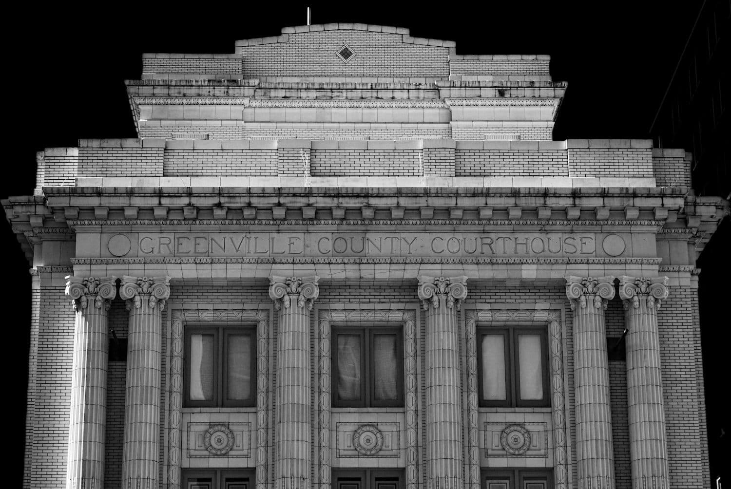 Black and white photograph of the Greenville County Courthouse facade, its name carved in stone above a row of ionic columns.