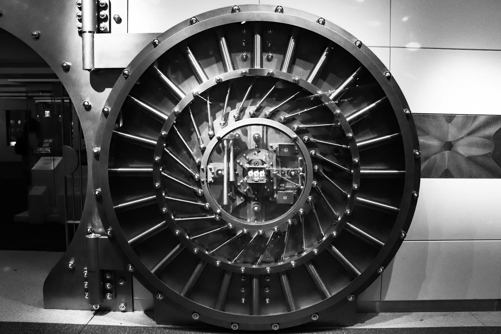 Black and white photograph of a massive circular bank vault door with its steel locking mechanism exposed.