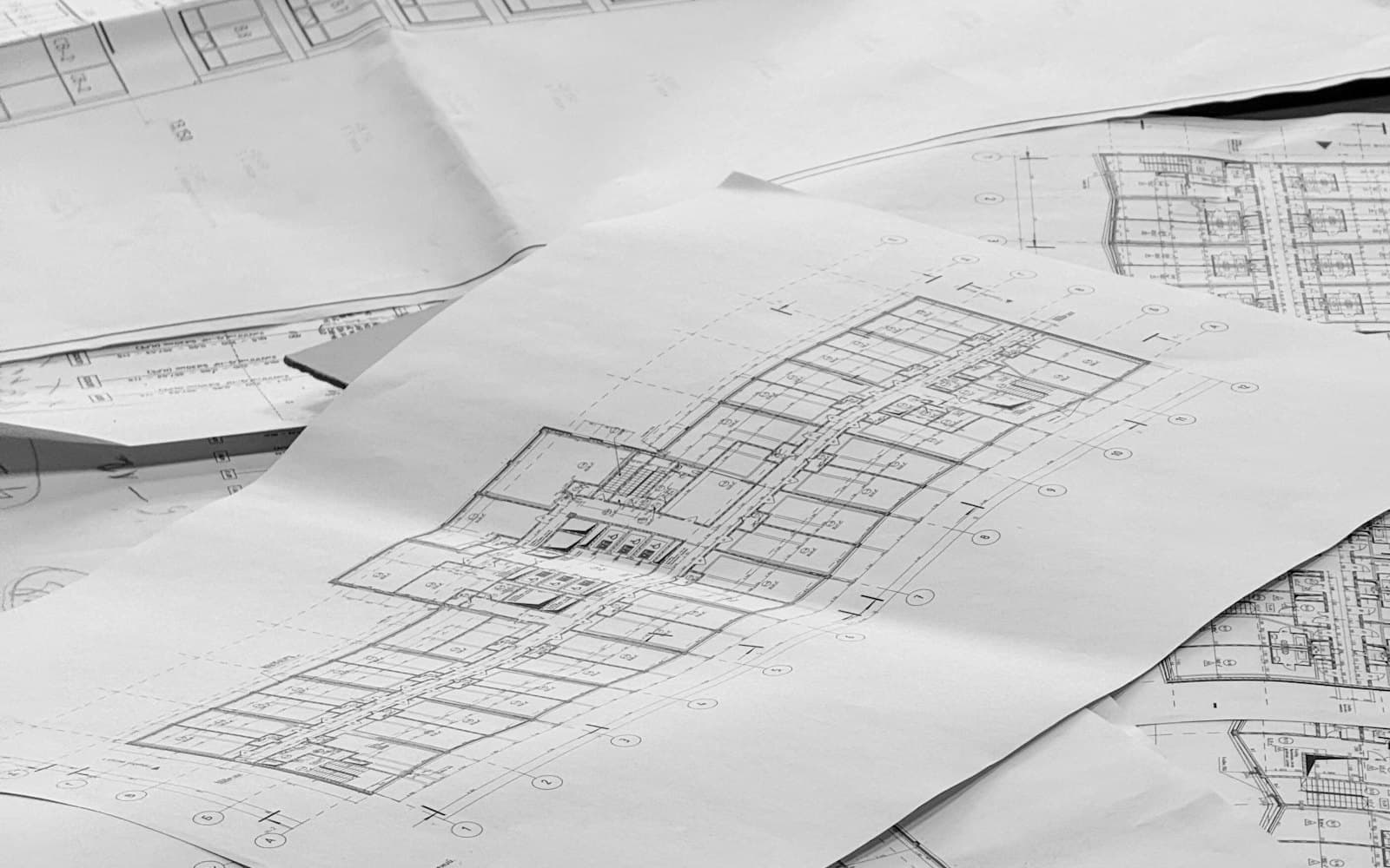 Black and white photograph of architectural floor-plan drawings spread across a table, dense with measurements and annotations.